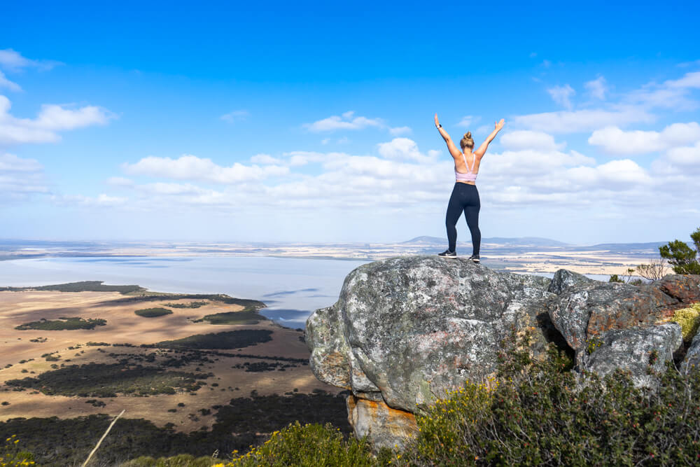 Gemma standing at the top of mount greenly in south australia with her hands in the air