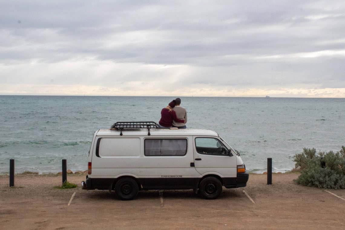 A couple sitting on a campervan overlooking the sea