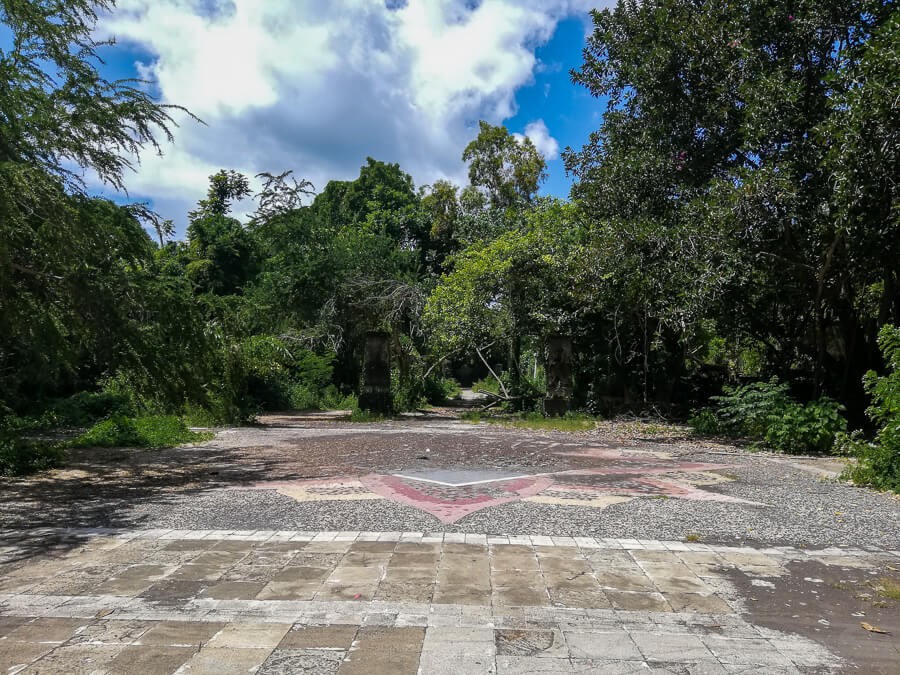 Nature reclaims the ruins of the abandoned theme park as trees and bushes overgrow the paths.