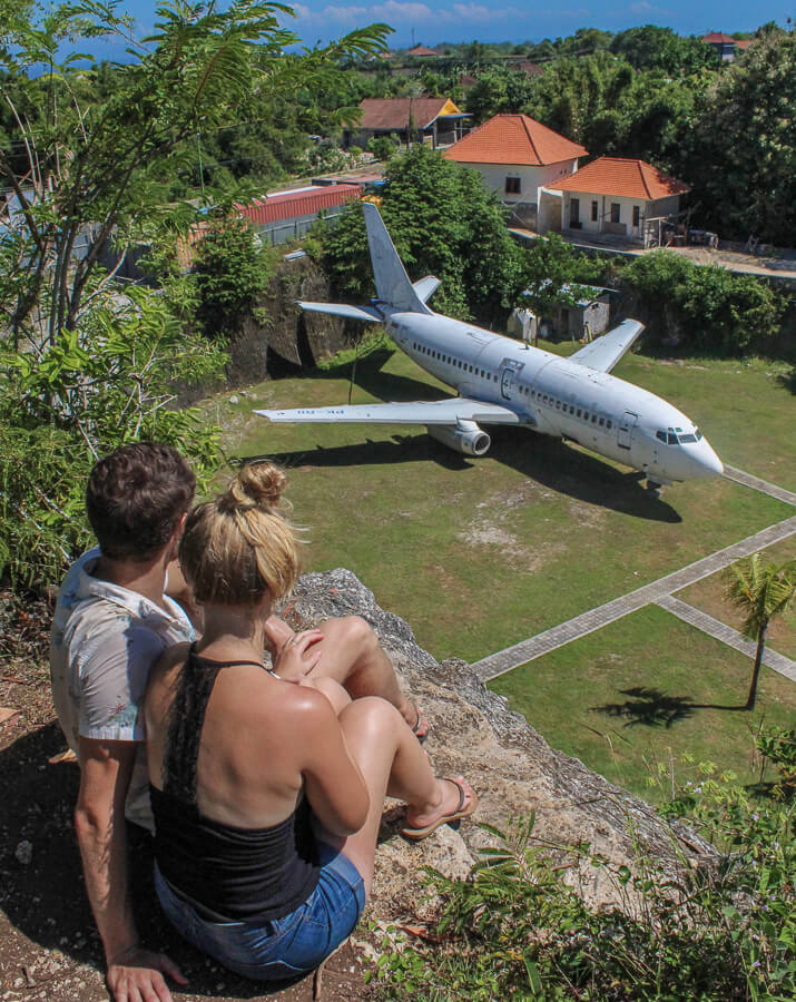Couple sitting on a cliff with a view of the abandoned plane sitting in a field.