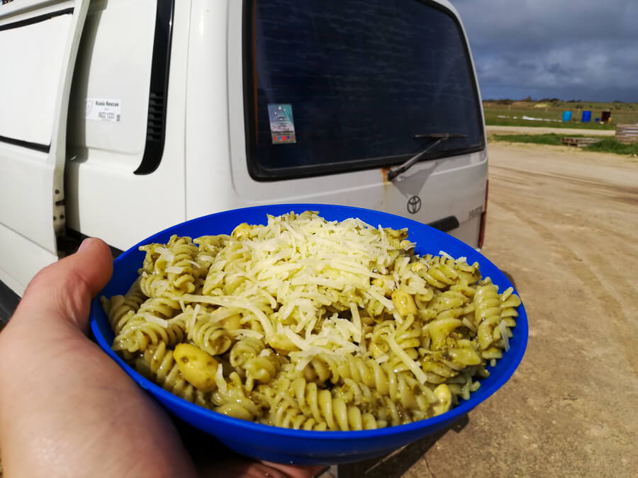 A bowl of pesto pasta and a topping of parmesan.