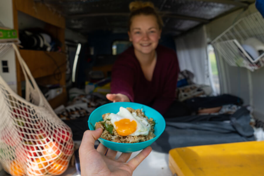 Handing a bowl of Nasi Goreng to Gemma, who is sitting inside a campervan