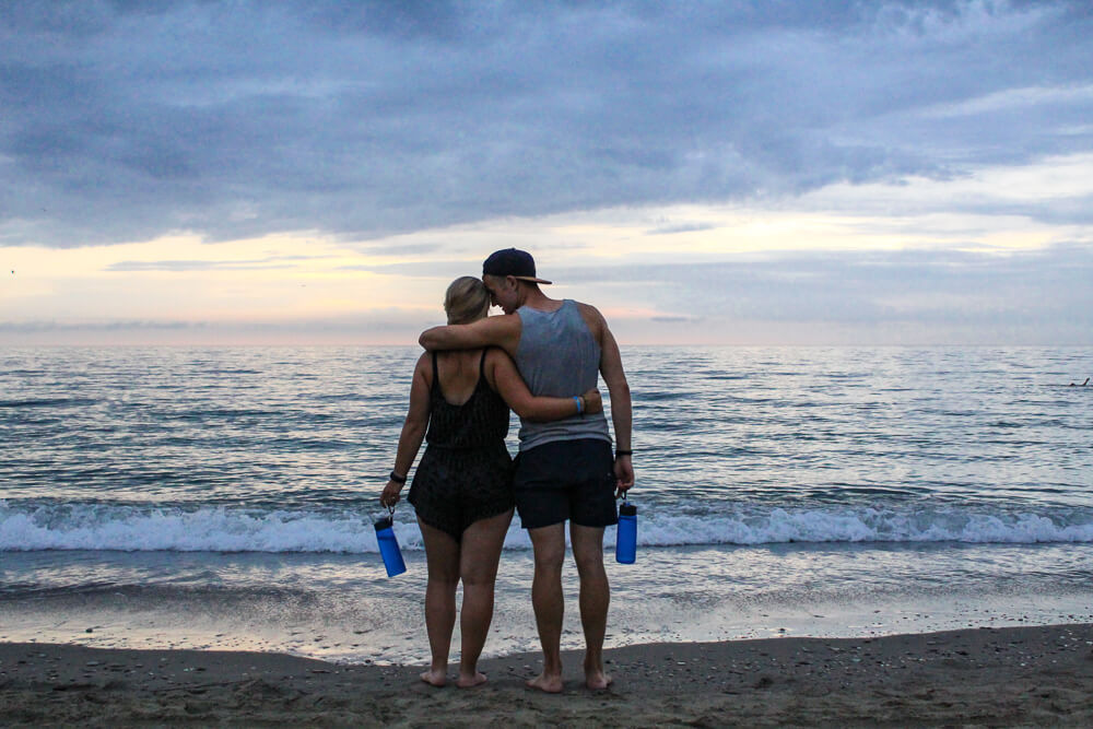 gemma and campbell standing on a beach at sunset holding lifestraw filter waterbottles
