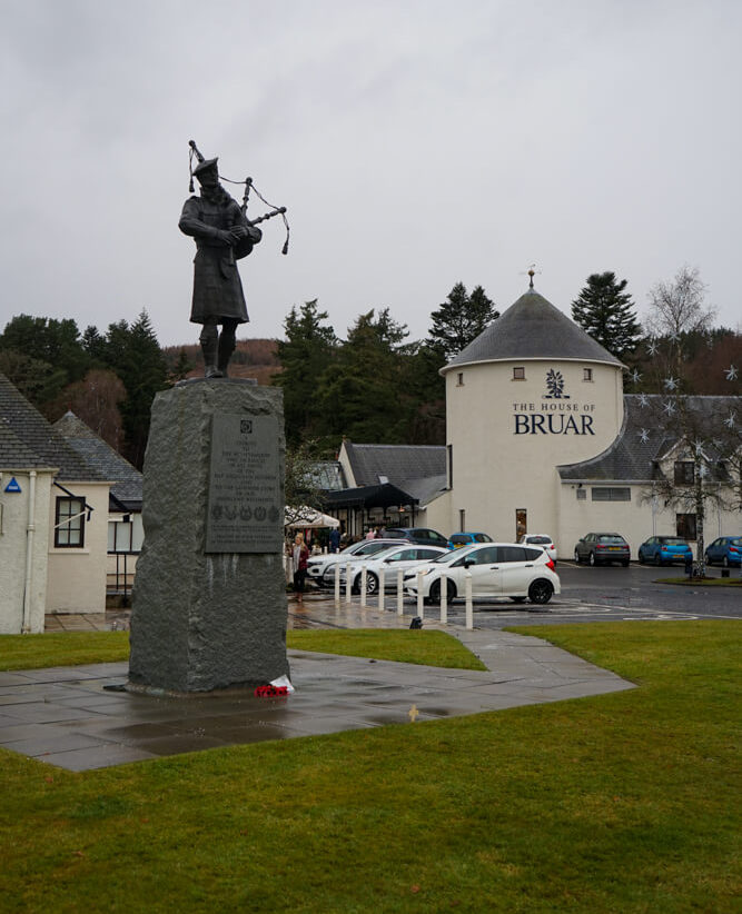 monument of a man playing bagpipes infront of white building