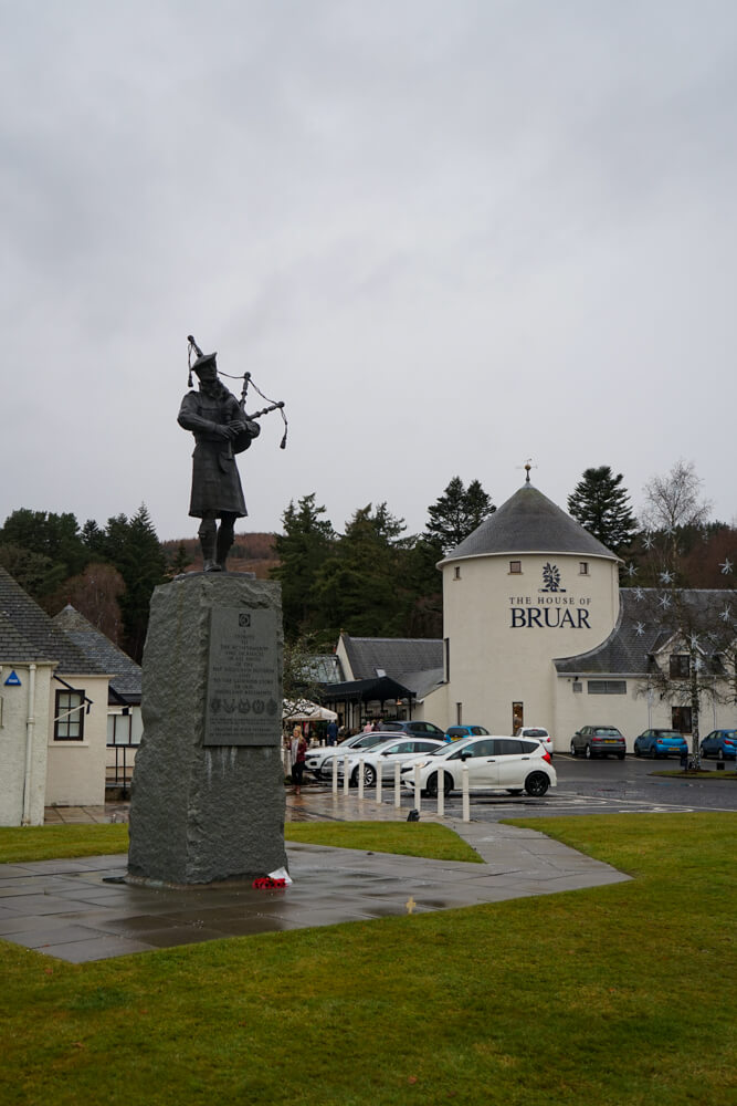 monument of a man playing bagpipes infront of white building