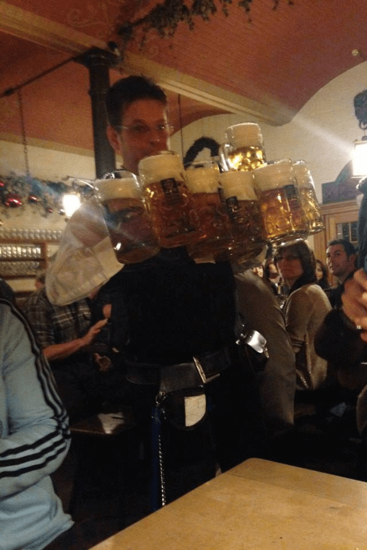 man holding lots of beer in a beer hall in munich